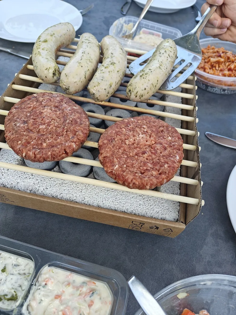 Twee kinderen helpen bij het omdraaien van hamburgers en worstjes op de Big Jeff wegwerpbarbecue