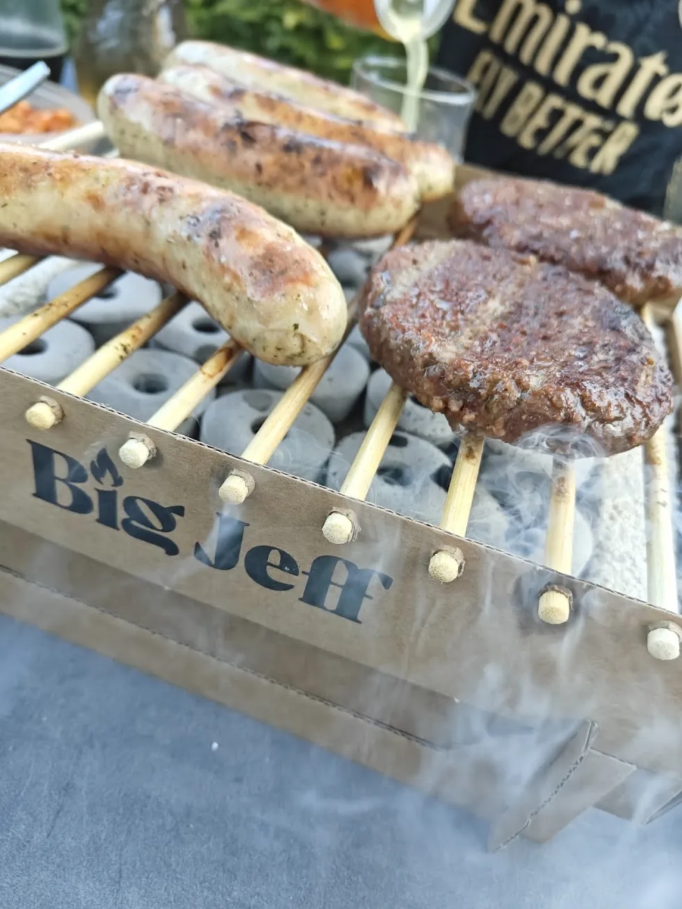 Close-up van worstjes en hamburgers op de Big Jeff wegwerpbarbecue, met rook die opstijgt